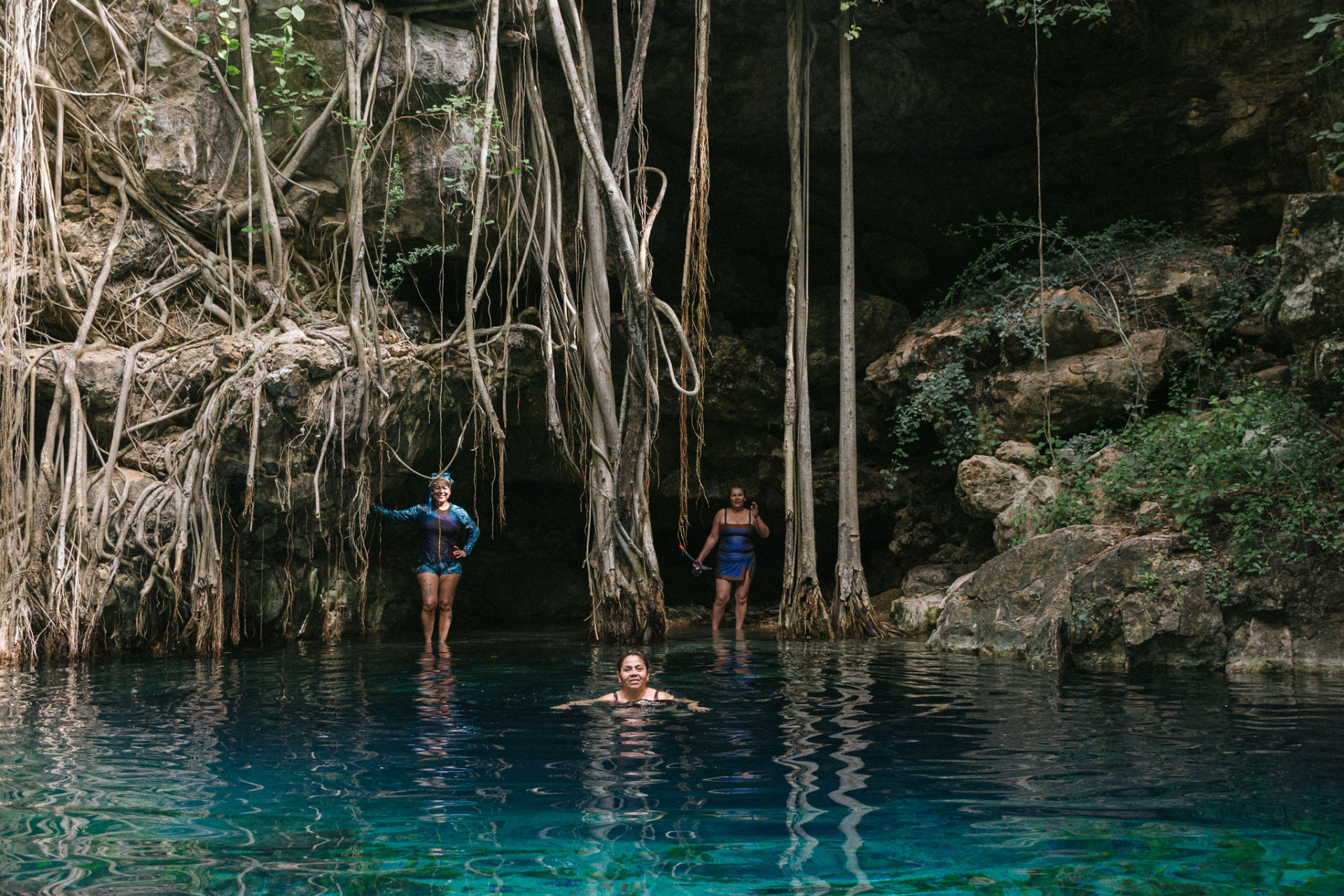 Viajeras nadando en un cenote de aguas turquesa rodeado de raíces y roca